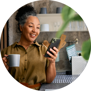 Black woman smiling while looking at her phone and holding a mug.